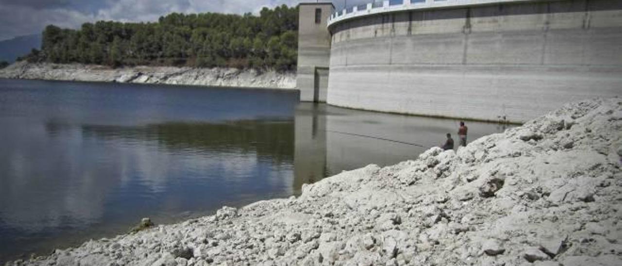 Dos pescadores ante la presa del pantano de Beniarrés, donde queda en evidencia que el nivel del agua se encuentra muy bajo.