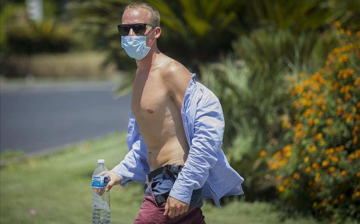 Un hombre con el torso descubierto y gafas de sol camina por la calle en Sevilla.