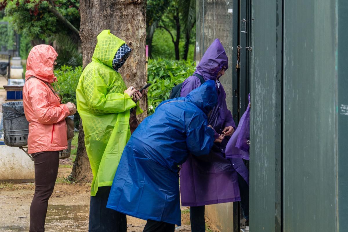 Varias personas se protegen de la lluvia con chubasqueron en Sevilla.