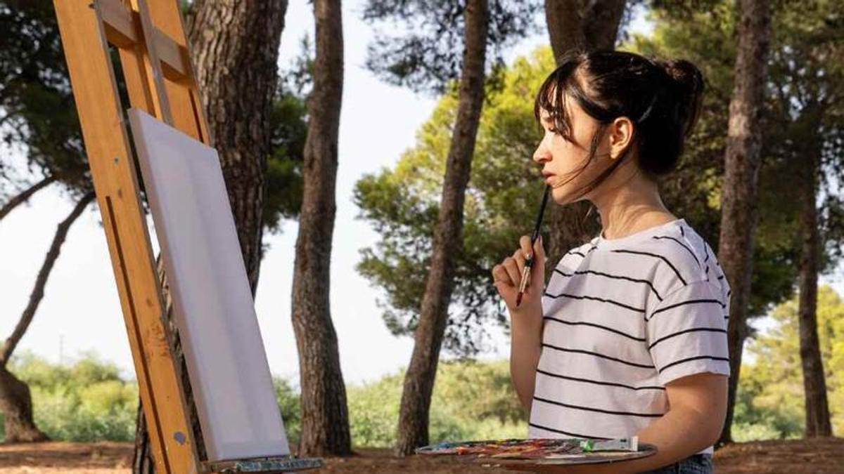 Una joven plantea una pintura sobre lienzo en una imagen de archivo.