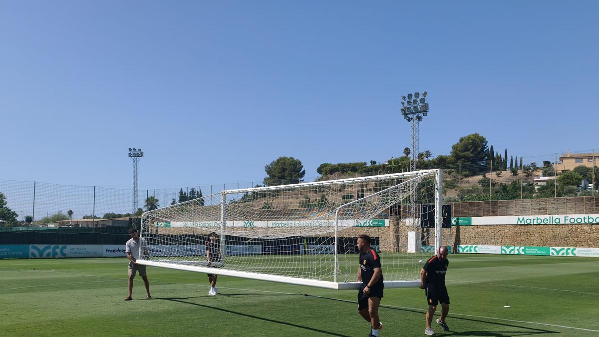El periodista José Peña, de blanco, ayuda a los trabajadores del Mallorca a mover la portería en el Marbella Football Center.