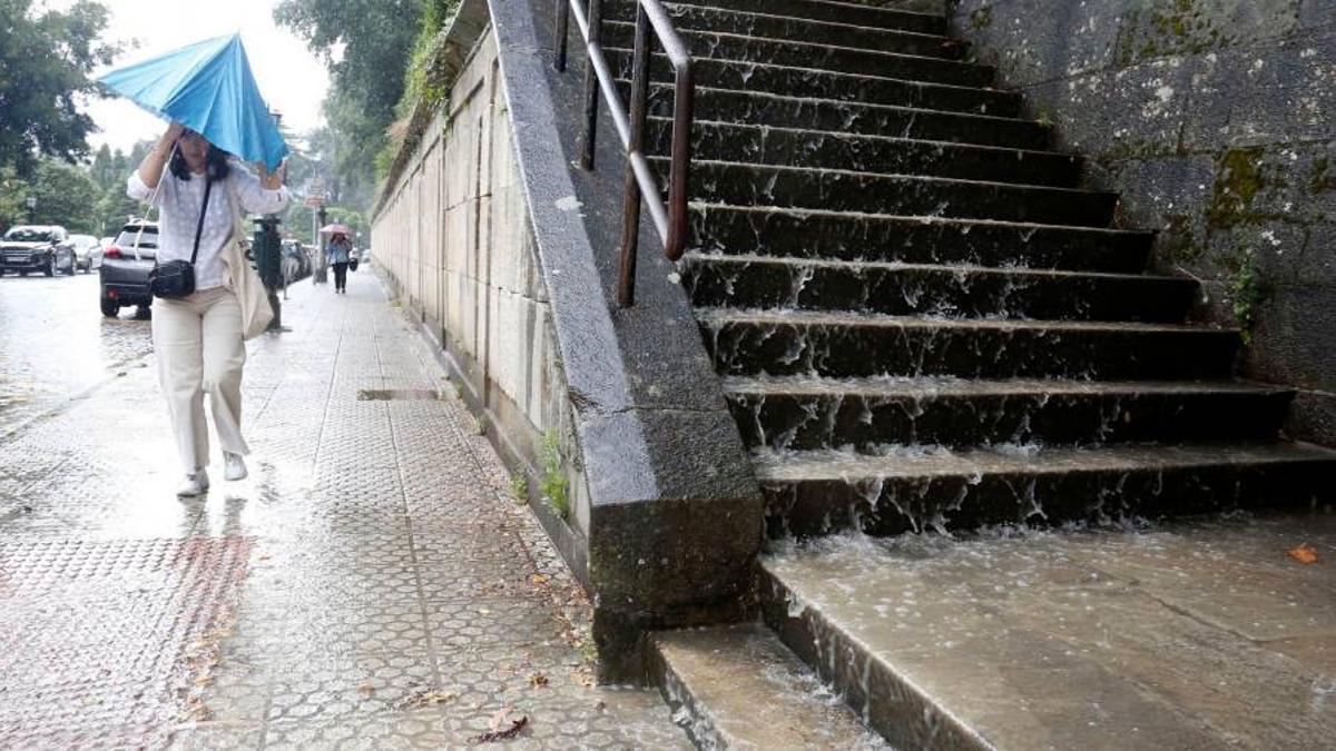 Una viandante intenta cubrirse durante uno de los chaparrones de estos días en Santiago