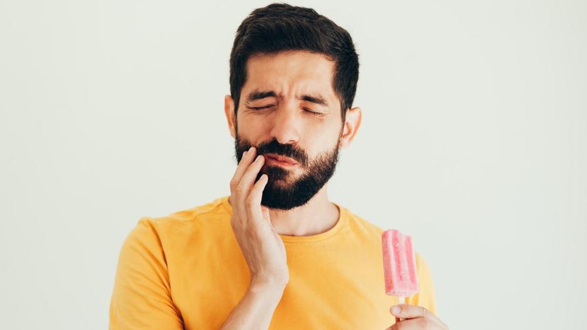 Un hombre sufre sensibilidad dental al comer un helado.