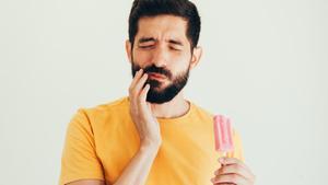 Un hombre sufre sensibilidad dental al comer un helado.