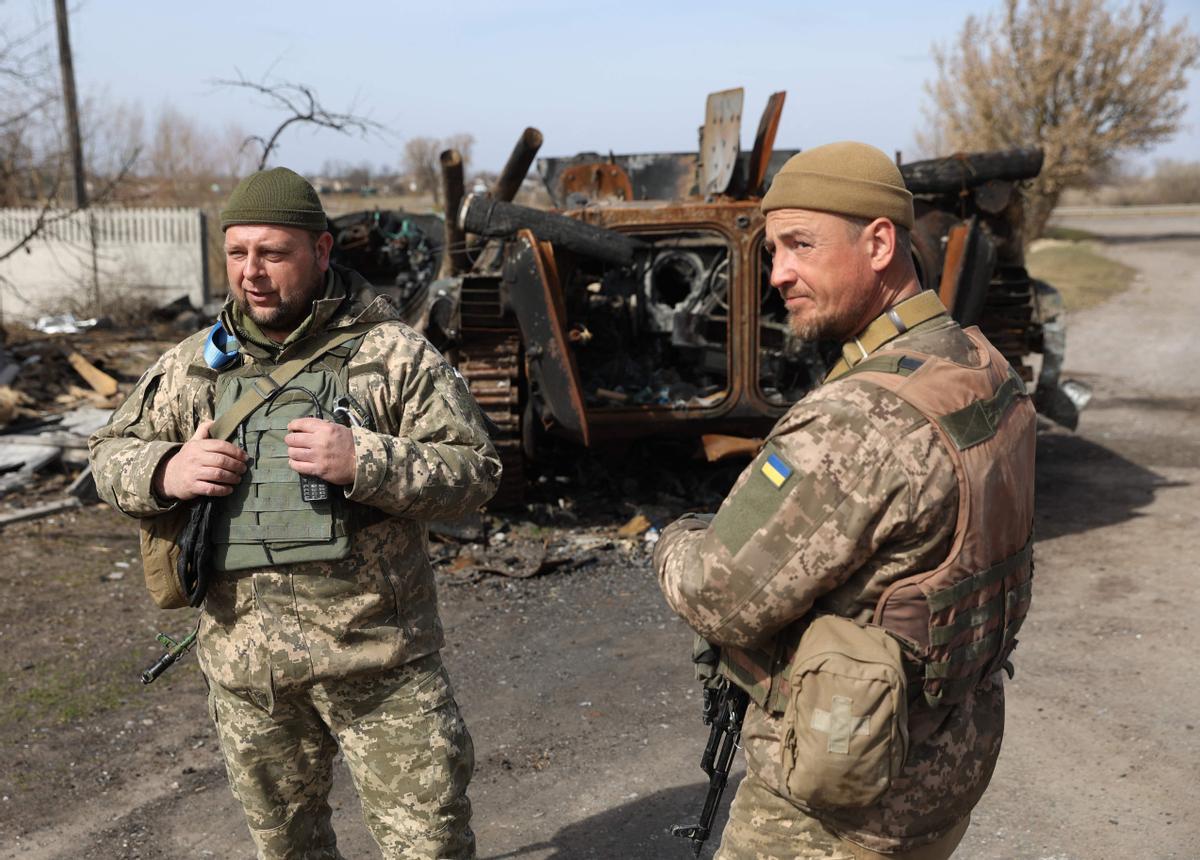 Soldados ucranianos se paran frente a un vehículo blindado personal (APC) ruso destruido en la línea del frente en la parte norte de la región de Kiev