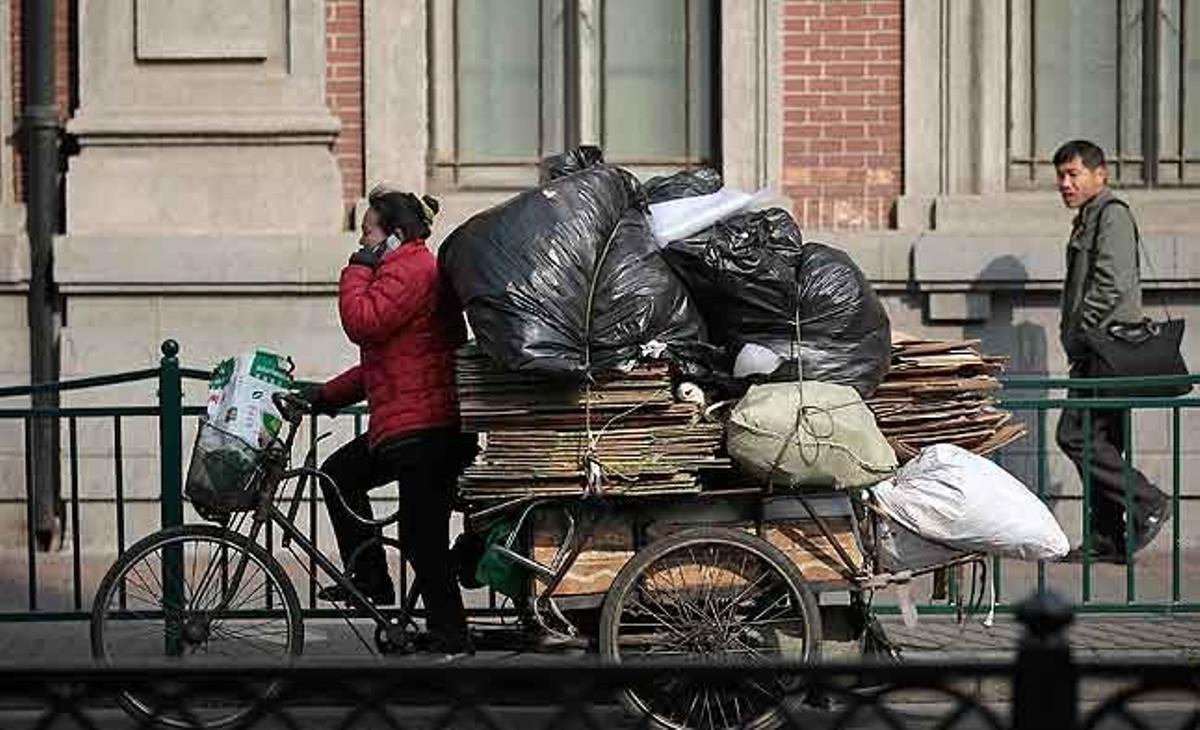 Una escombriaire condueix el seu tricicle carregat de material reciclable mentre parla pel telèfon mòbil, a Xangai (Xina).