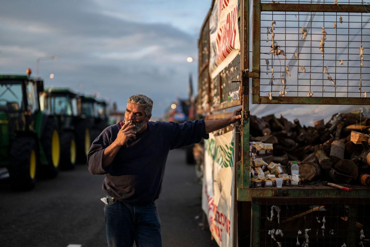 A farmer smokes as he stands among the tractors blocking the national highway outside the central Greek city of Karditsa on December 8, 2025. Greek farmers demanding the payment of EU subsidies on December 8 shut down the two main international airports on the island of Crete after clashing with riot police in a growing showdown with the government. (Photo by Aris MESSINIS / AFP)