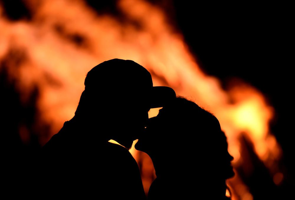 Una pareja se besa frente a las tipicas hogueras de la noche de San Juan.