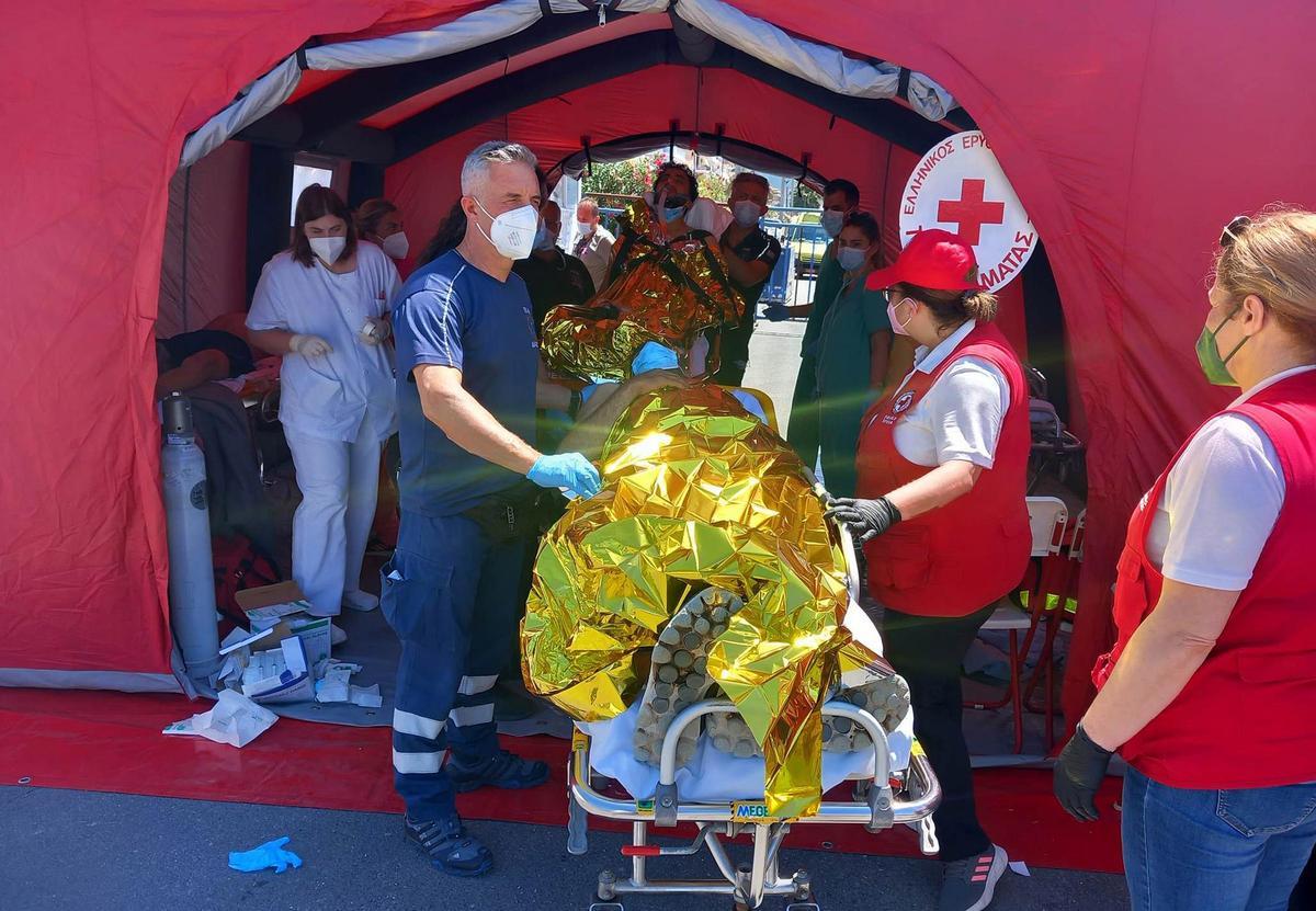 Paramédicos del Servicio Nacional de Ambulancias de Emergencia de Grecia (EKAV) y miembros de la Cruz Roja griega ayudan a migrantes supervivientes del hundimiento de un pesquero en su llegada en el puerto de Kalamata.