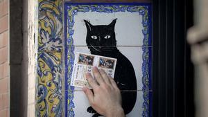 Un hombre pasa dos décimos de la Lotería de Navidad por el popular azulejo de la administración de loterías El Gato Negro en Sevilla.