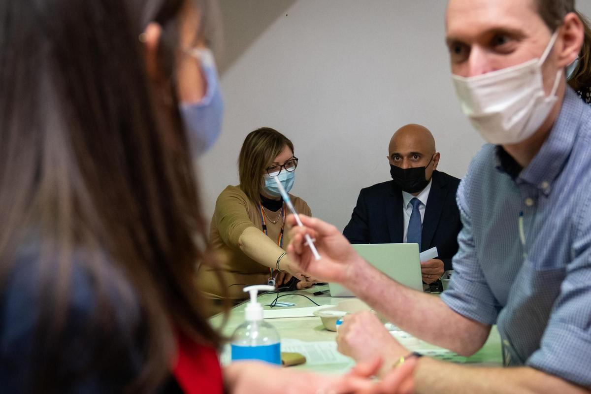 El ministro de Sanidad de Reino Unido, Sajid Javid, ayuda a rellenar los datos de la paciente Amie Stott, que recibe su vacuna de refuerzo, durante una visita al centro de vacunas de Abbey, en el centro de Londres.