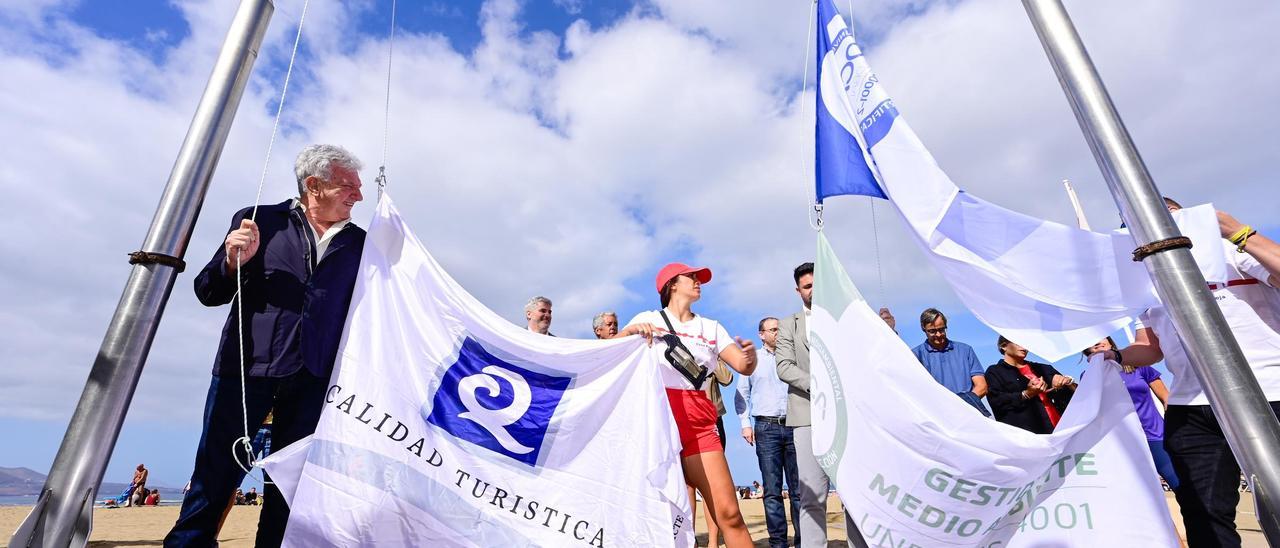 De izquierda a derecha, Pedro Quevedo y Héctor Alemán, con traje gris, izan las banderas en la playa de Las Canteras, acompañados por diversos colectivos este viernes..