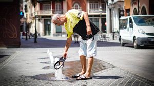Una persona sin hogar moja su gorra en una fuente de la plaza de la Soledad de Badajoz para refrescarse