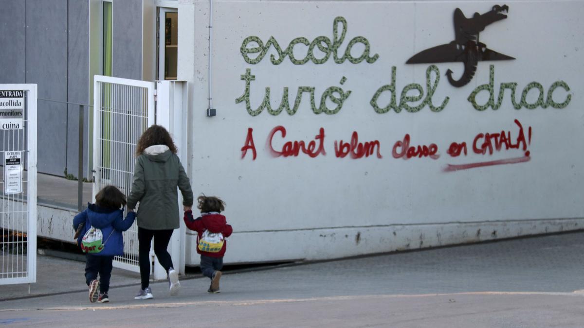 Una mare acompanya els seus fills a l&#039;escola Turó del Drac de Canet de Mar. Una pintada reclama l&#039;ensenyament en català a la façana del centre