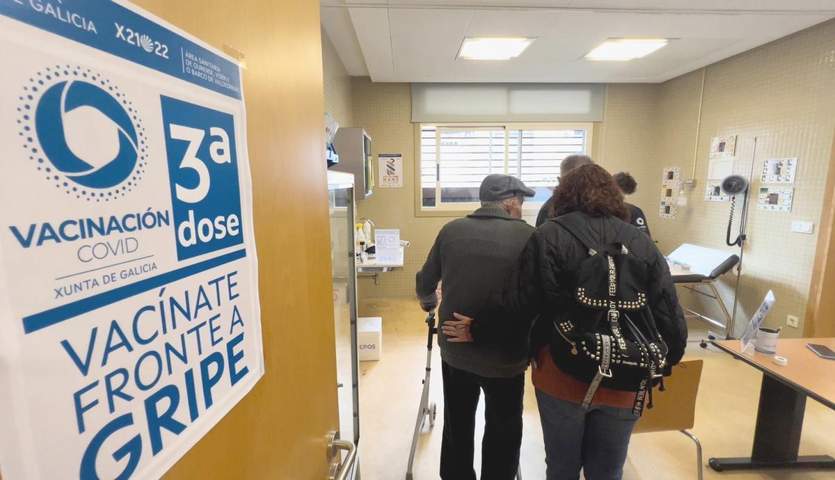 Una mujer acompaña a un mayor que va a recibir la tercera dosis de la vacuna, en el centro de salud de Maceda.