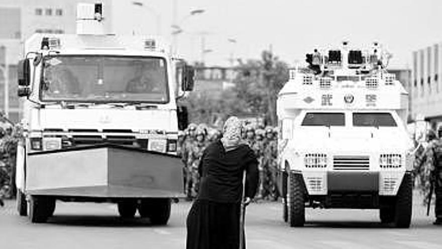 Una mujer uigur, ante dos vehículos militares en la ciudad de Urumqi.