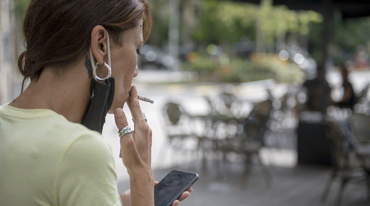 Una mujer fuma a cierta distancia de las mesas de la terraza de un bar de Barcelona, el pasado 18 de agosto.