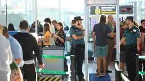 Un usuario pasa bajo el arco de detección de metales de la T-1 del aeropuerto de El Prat ante la mirada de dos guardias civiles. 