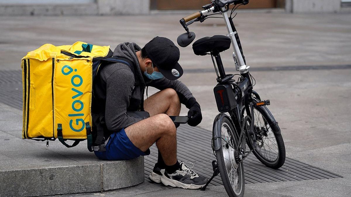 Un repartidor de Glovo revisa sus mensajes en el móvil en una plaza de Madrid, el pasado 30 de abril, en plena pandemia