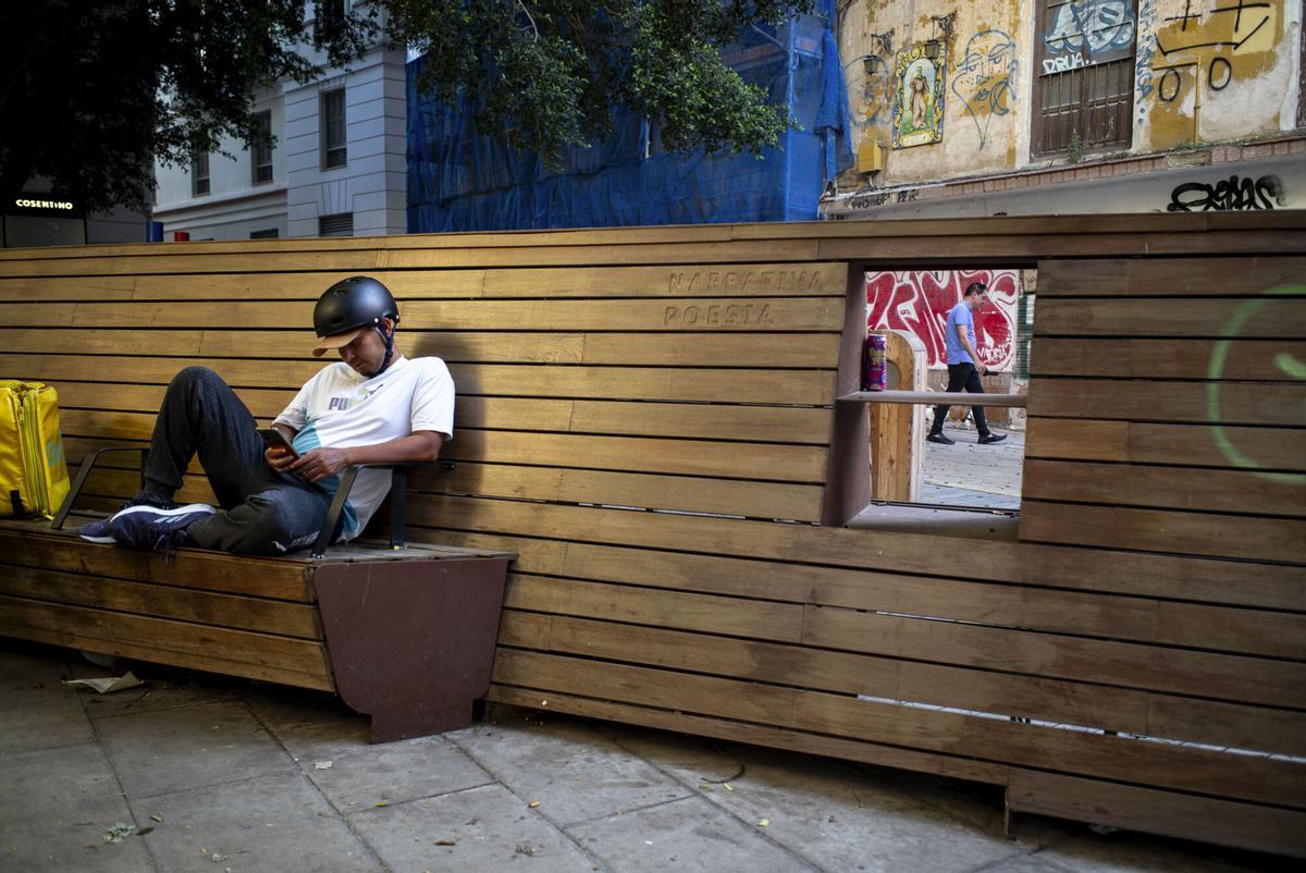 Un repartidor de comida rápida descansa en un banco de la Plaza de San Pedro de Alcántara, en Málaga