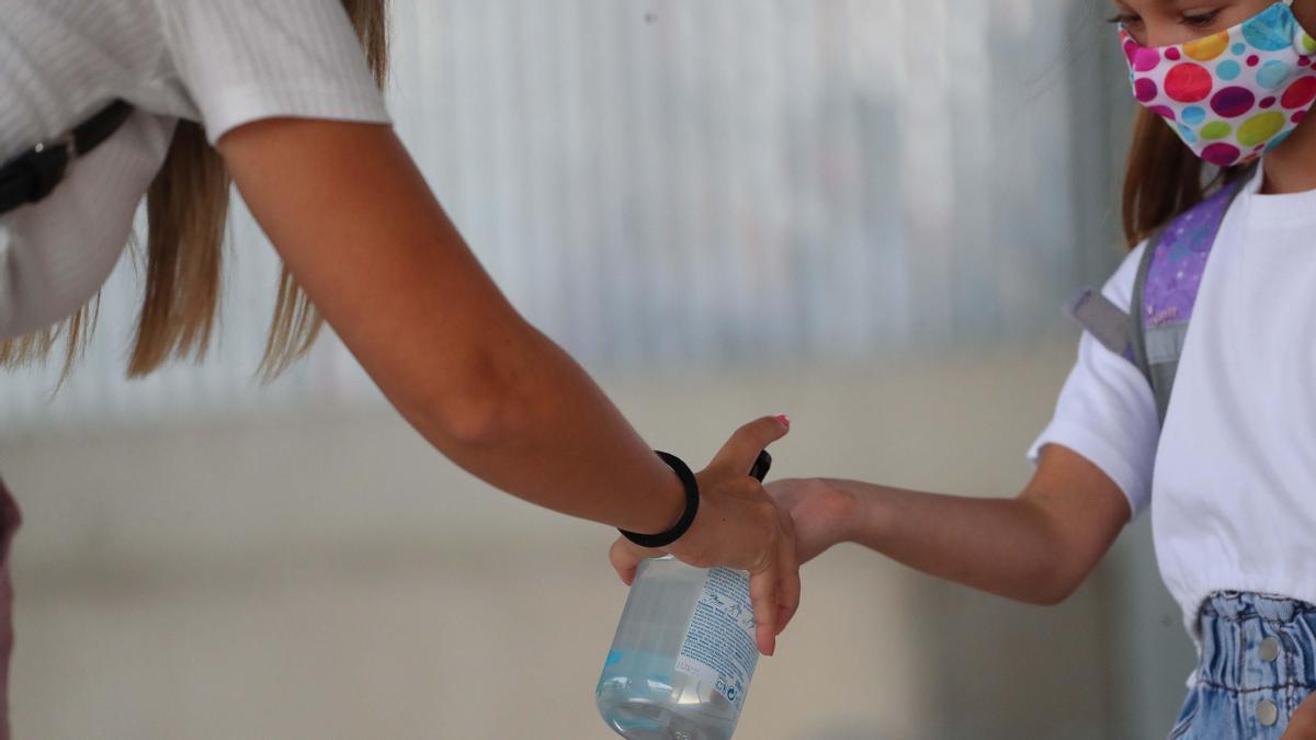 Una docente ofrece gel a una escolar.