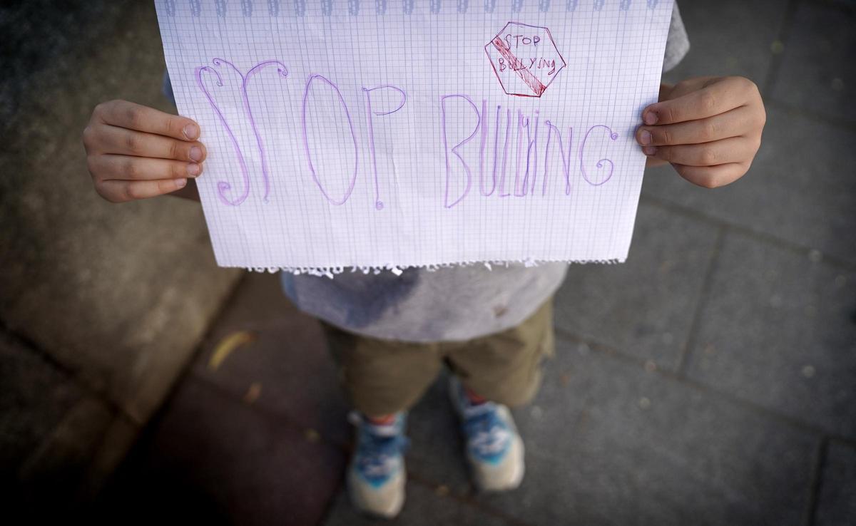 Un niño de primaria sostenie un cartel contra el bullying, a la salida de su colegio.