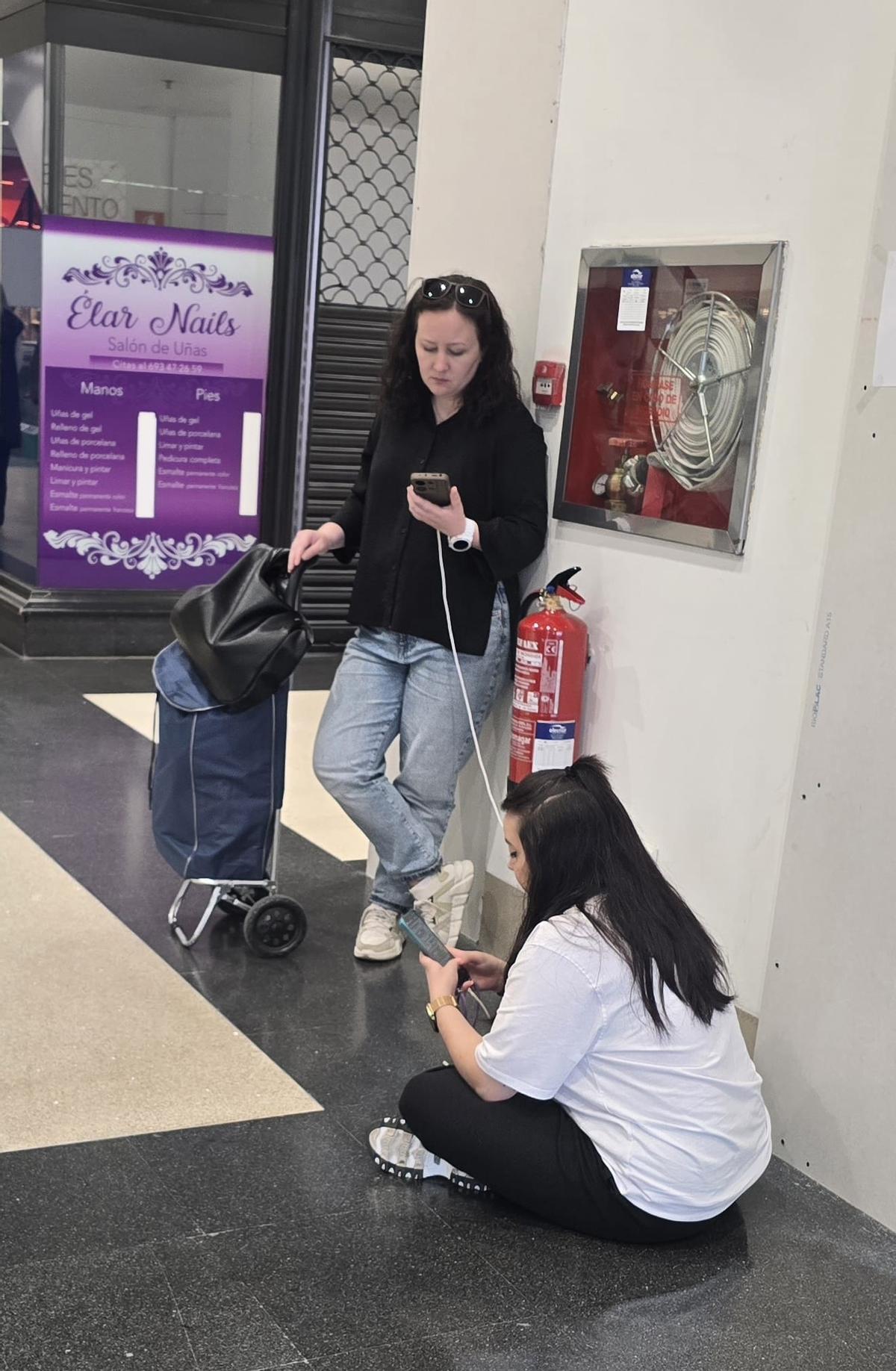 Dos mujeres cargando sus móviles en el Centro Comercial Arousa, ayer.