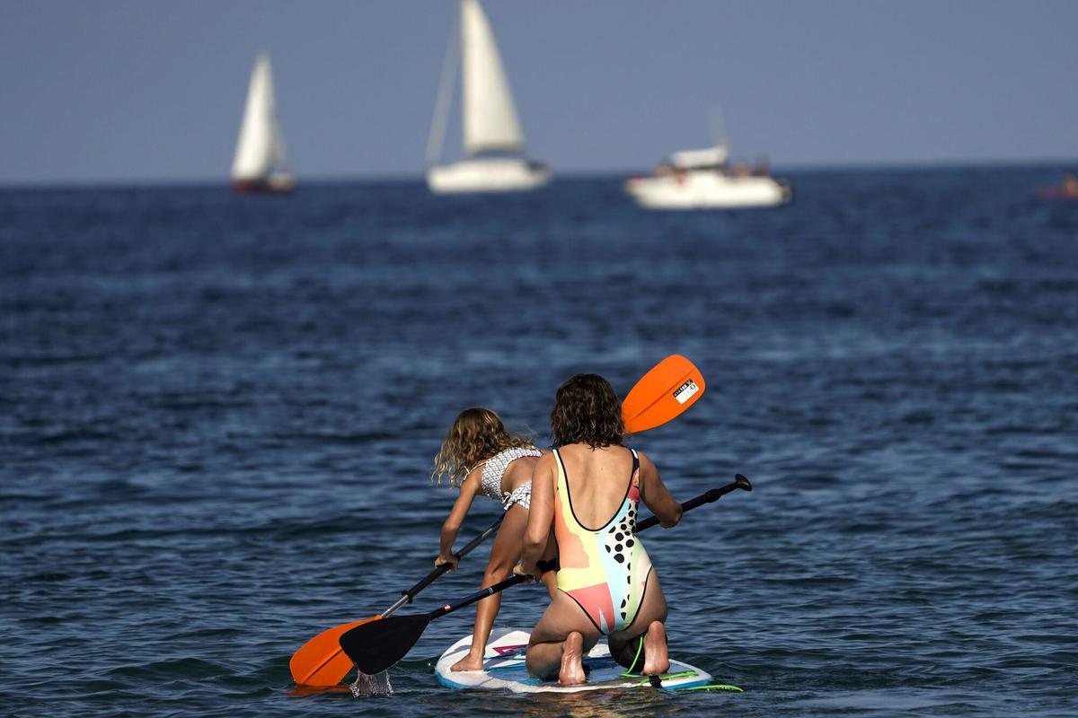 Bañistas con una tabla de paddle surf en la playa de La Ribera, en la localidad asturiana de Luanco