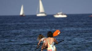 Bañistas con una tabla de paddle surf en la playa de La Ribera, en la localidad asturiana de Luanco