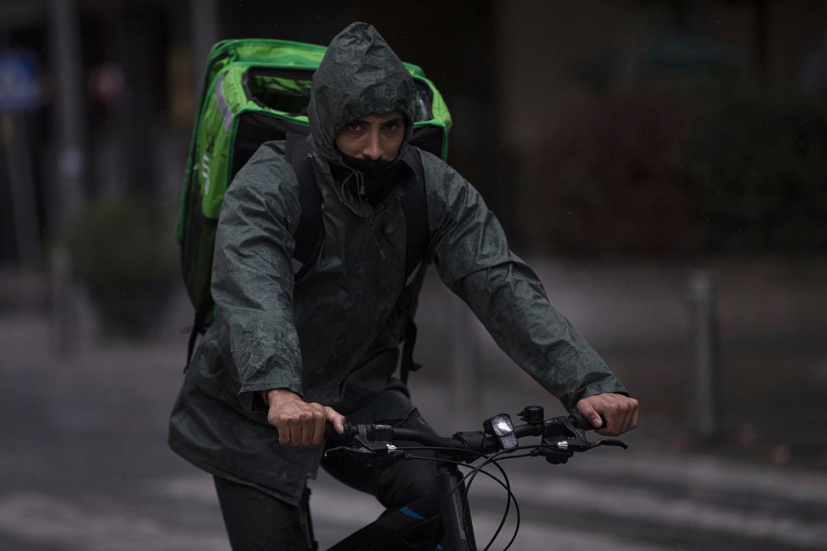 Un rider (repartidor) trabaja bajo la lluvia protegido con un impermeable