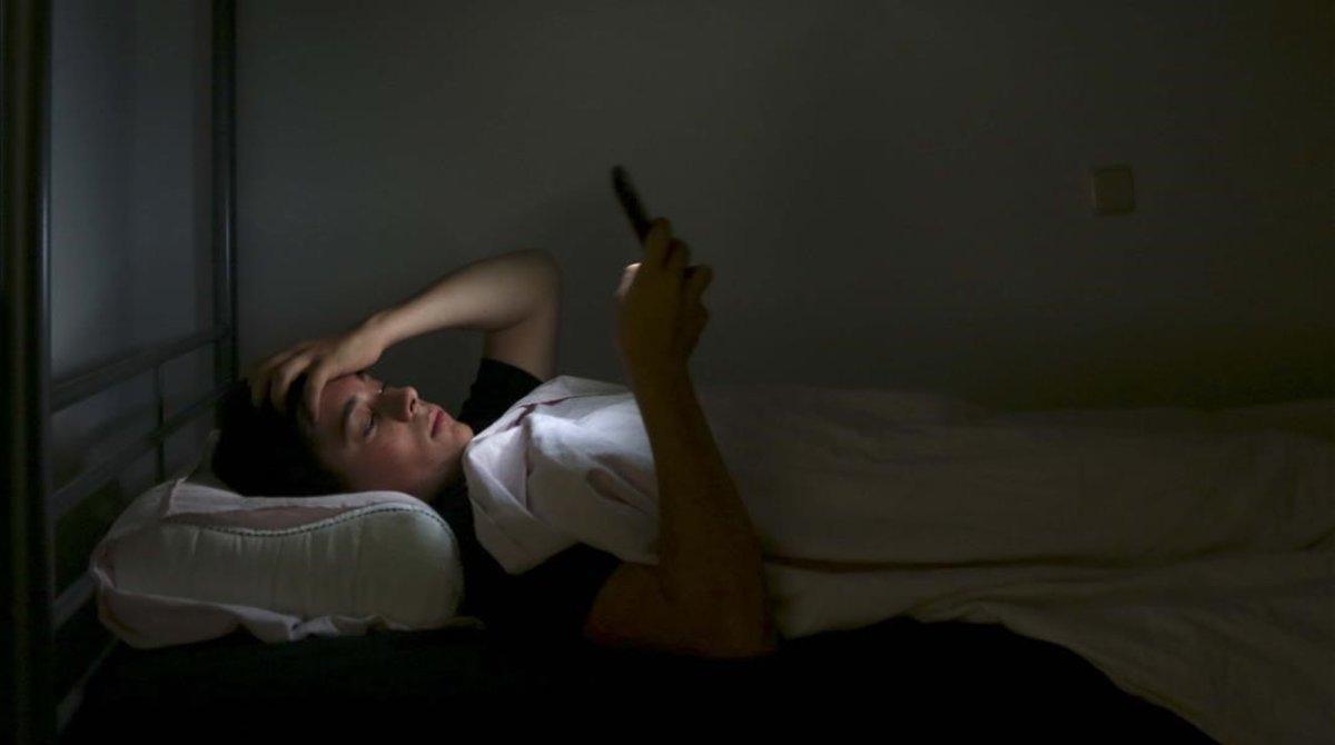 Un adolescente de 15 años no concilia el sueño y mira su móvil tumbado en su cama.