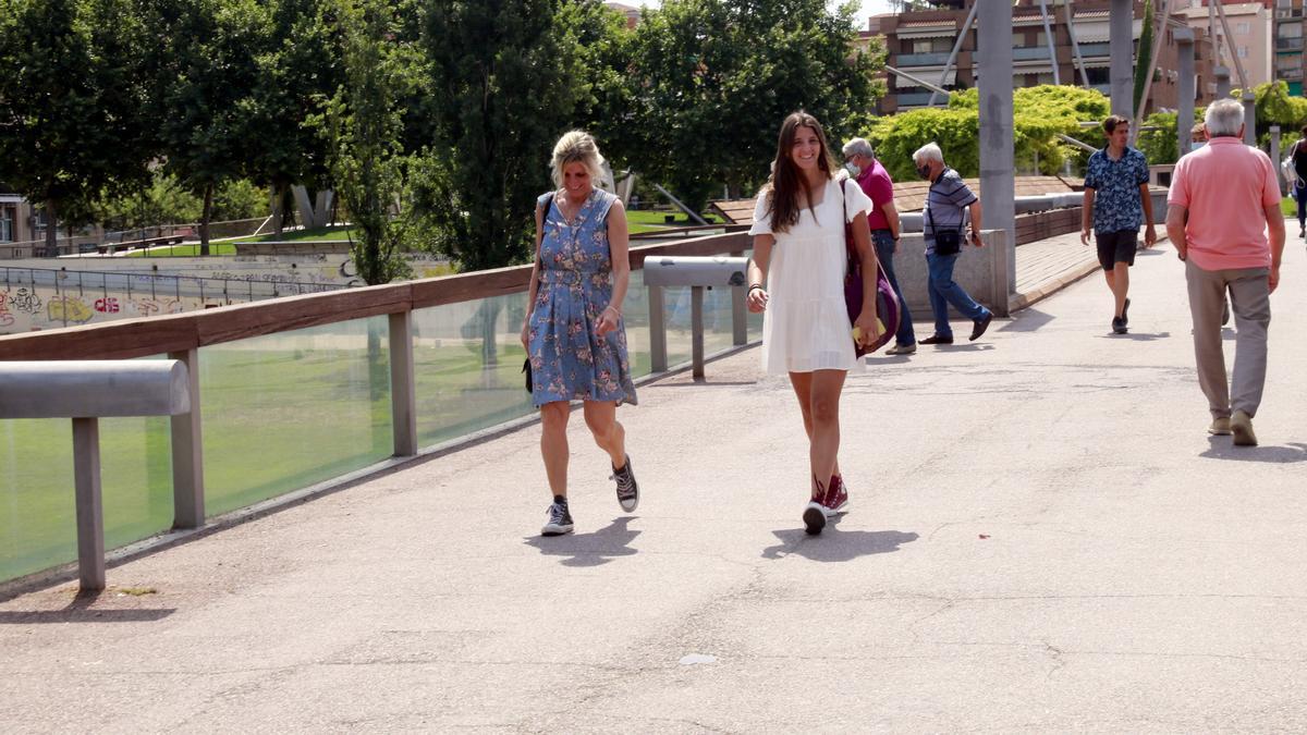Pla obert de dues noies sense mascareta passejant per la passarel·la del riu Segre a Lleida en el primer dia sense l&#039;obligatorietat de dur-la a l&#039;exterior, el 26 de juny de 2021. (Horitzontal)