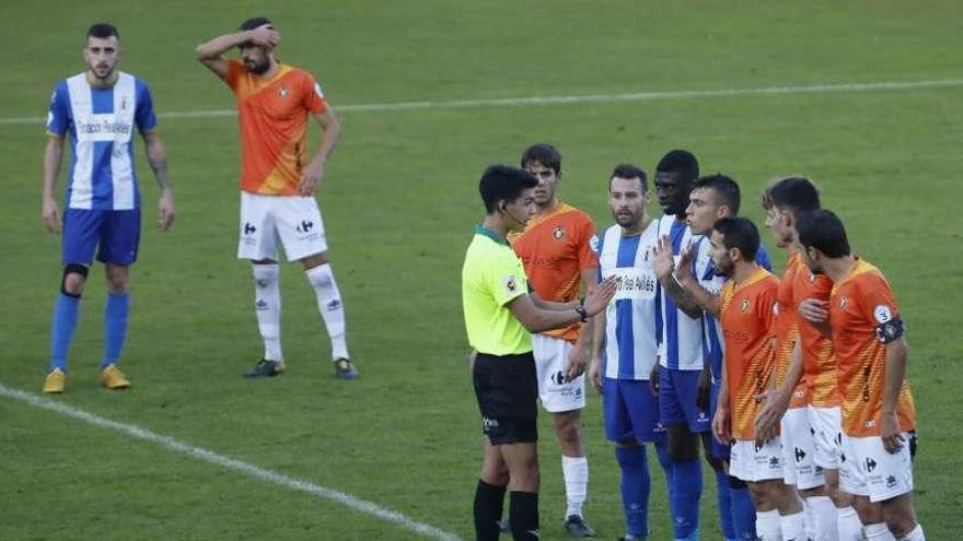 El colegiado conversa con Barra, del Avilés, ante varios jugadores locales y del Caudal en la barrera.