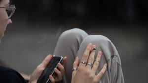 Imagen de una joven fumando mientras mira el móvil.