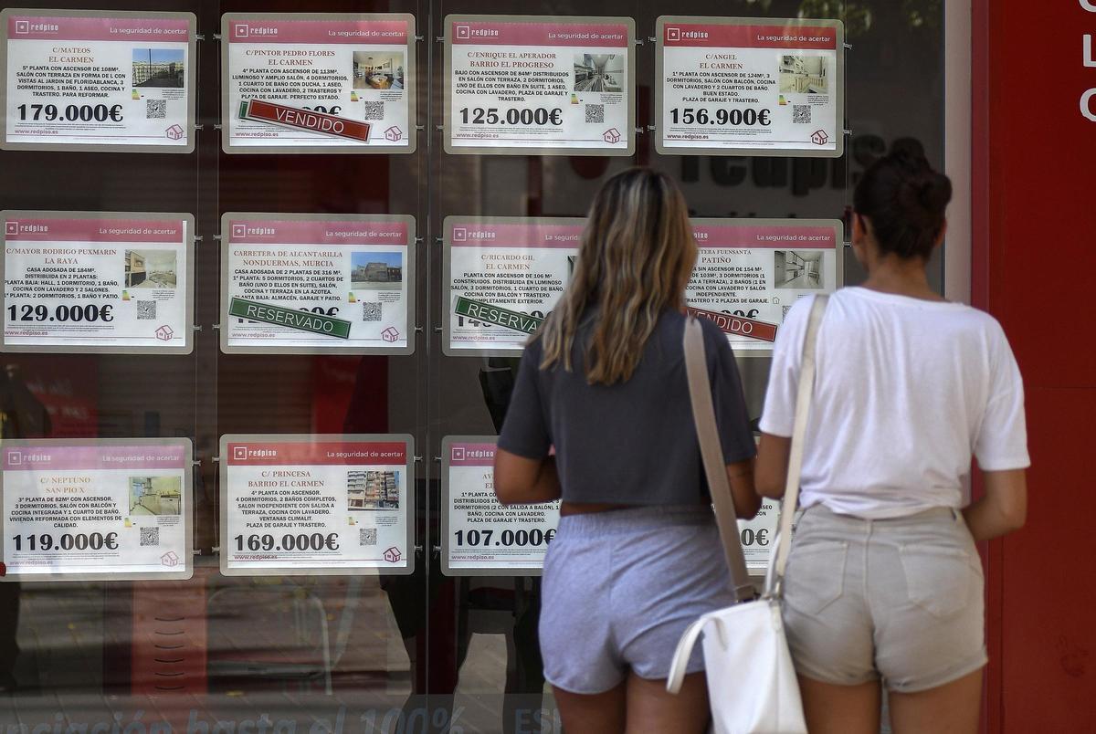 Dos jóvenes consultan los anuncios en el escaparate de una oficina inmobiliaria en Murcia.