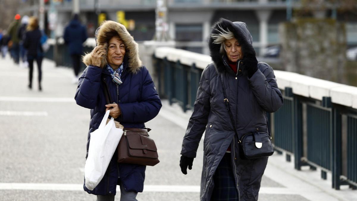 Dos mujeres se protegen del viento en el puente de Santiago de Zaragoza