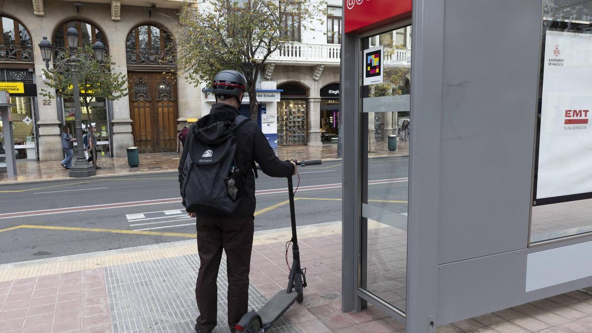 Un usuario de patinete espera a subir al bus, junto a una parada de la EMT.