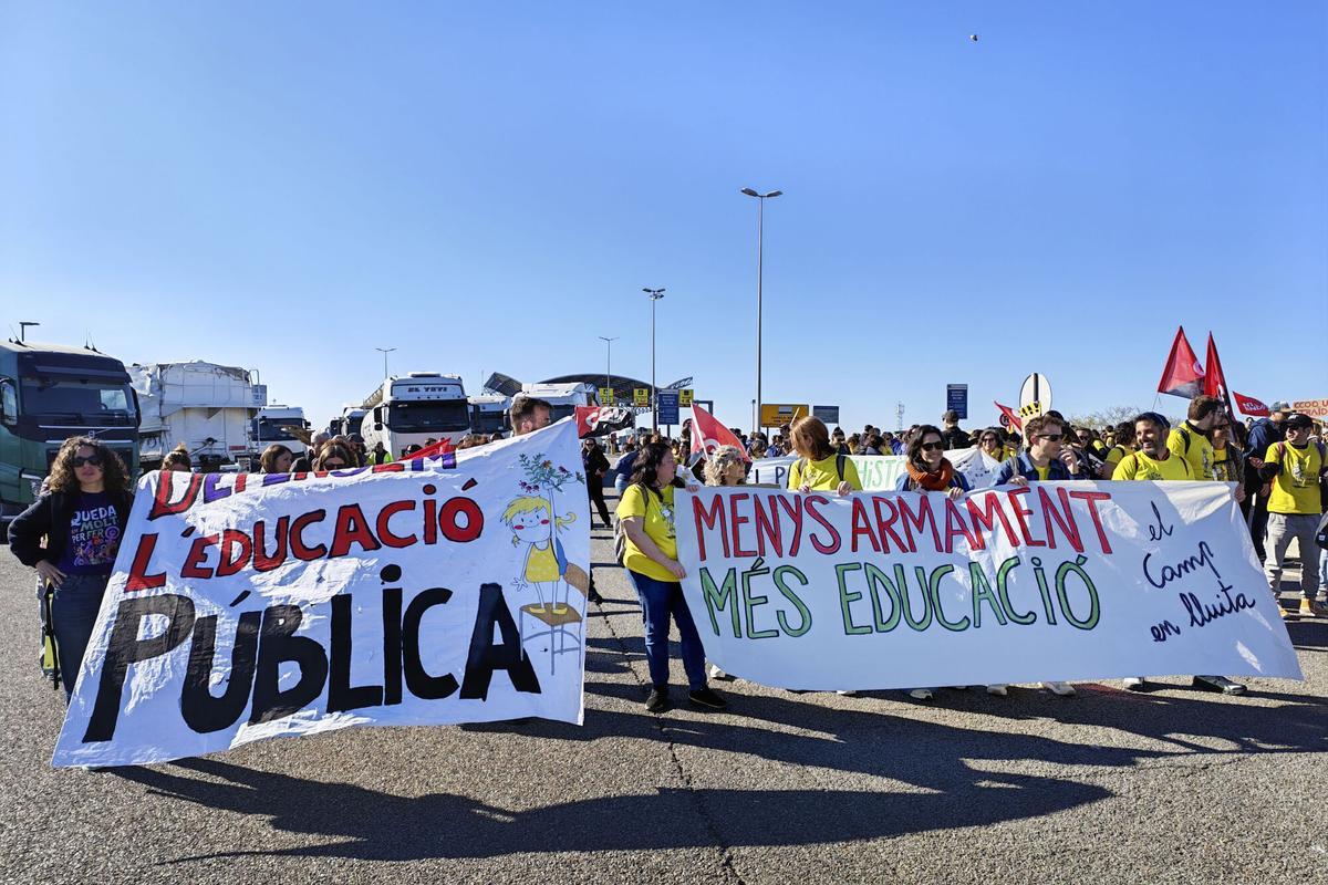 Varios docentes sostienen dos carteles con los mensajes: "Defendamos la educación pública" y "Menos armamento y más educación", en la huelga de profesores.