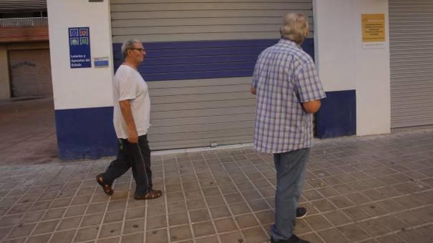 Dos hombres pasan ante la administración El gato negro de Mislata, ayer.