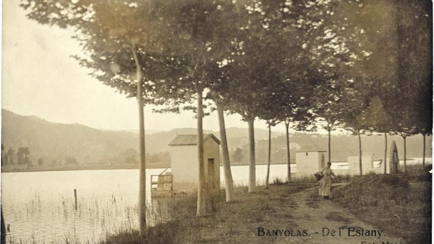 Postal de l&#039;estany amb una de les pesqueres tradicionals, la de Pere Rodríguez (Moner), amb balcó, i una dona al camí que voltava l&#039;estany