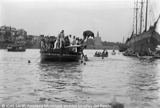 Un joven alcanza la bandera de la cucaña instalada en una barcaza en medio del río Gudalquivir. (1931)
