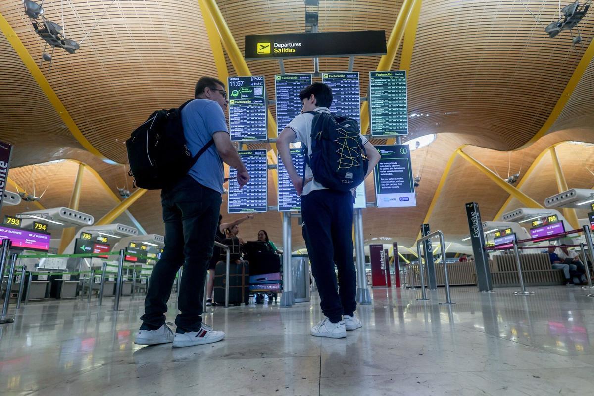 Dos personas observan el panel de salidas en el aeropuerto Madrid-Barajas.