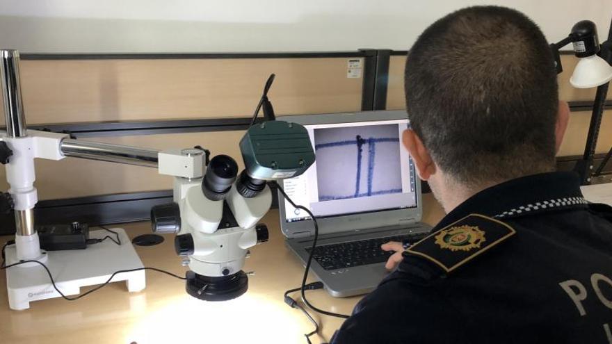 Un agente de la Policía Local de Elche examina al microscopio una firma para determinar su autoría, en una imagen de archivo
