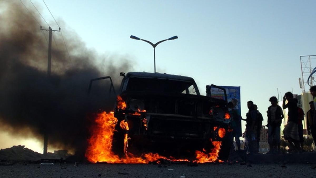 Yemenís se reúnen cerca de un vehículo incendiado propiedad de combatientes Huthi