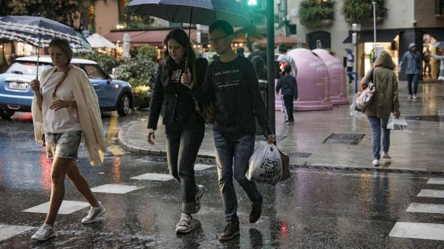 Unos transeúntes se guarecen de la lluvia bajo sus paraguas en Palma.