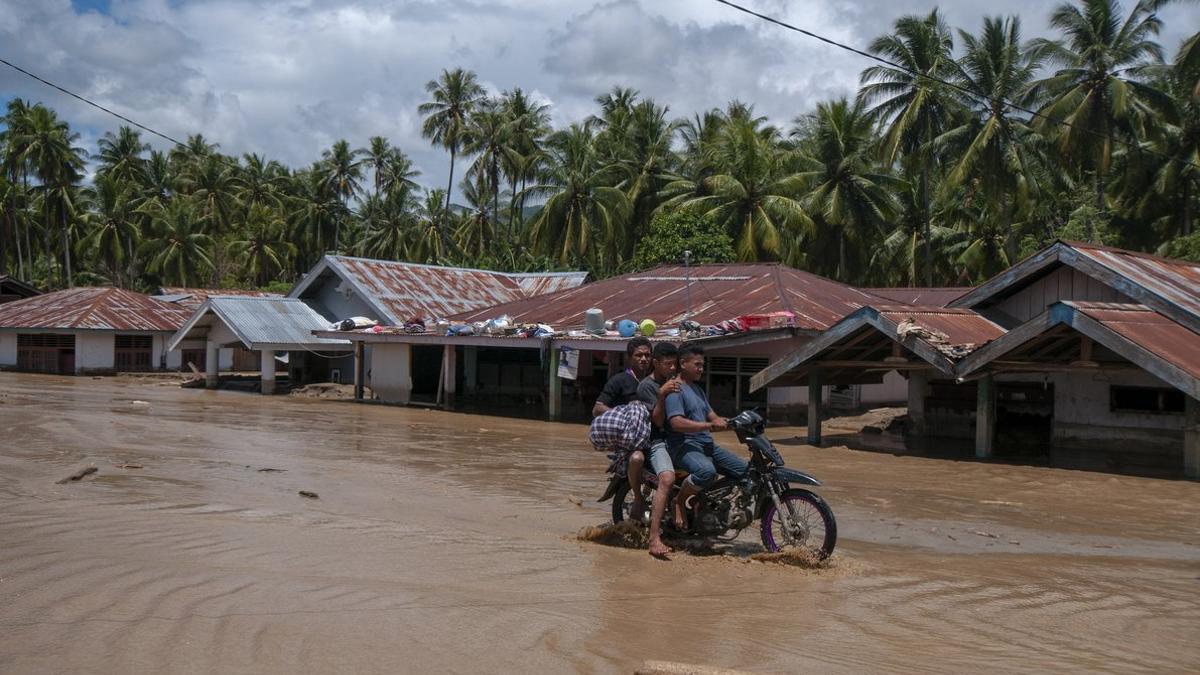 Unos jóvenes en motocicleta por una carretera inundada en Sumatra