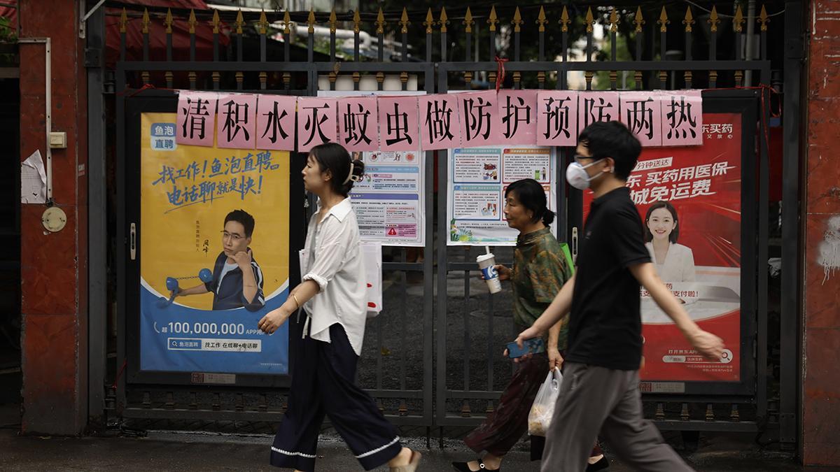 Ciudadanos pasan junto a una entrada de un edificio en la que se muestran avisos sobre el control de proliferación de mosquitos en Guangzhou, en la provincia china de Guangdong. El texto dice: "Trabajemos juntos para acabar con el agua estancada y la proliferación de los mosquitos".