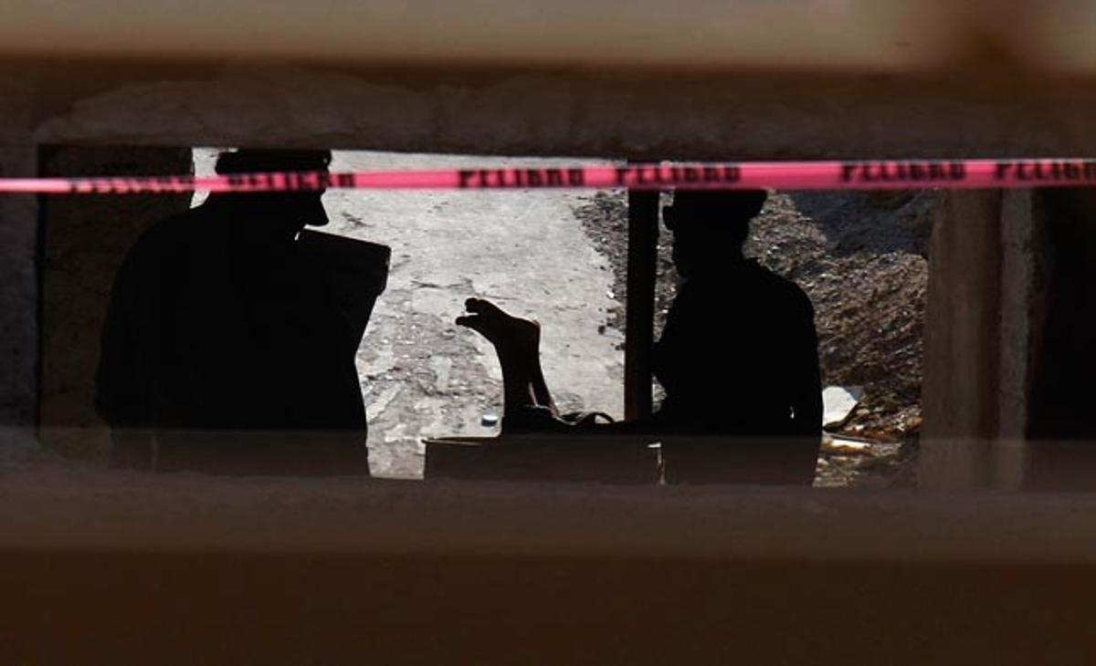 Unos policías mexicanos observan este lunes en Ciudad Juárez el cuerpo de una mujer asesinada, que ha sido encontrada bocabajo en un cubo de la basura.