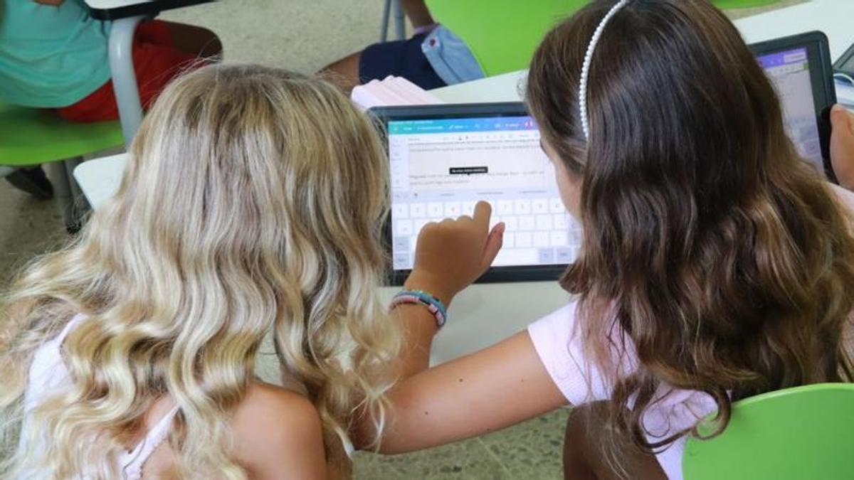 Dues nenes de Primària treballen amb una tauleta dins l’aula