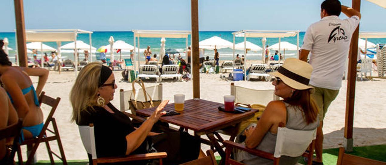 Dos amigas toman una aperitivo en la terraza de un chiringuito sobre la arena de la Playa de San Juan el verano pasado.